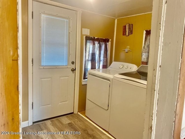 clothes washing area featuring washing machine and dryer, wooden walls, light wood-style flooring, and laundry area