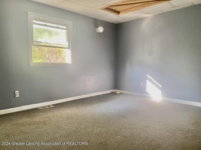 carpeted empty room featuring baseboards, visible vents, and a paneled ceiling
