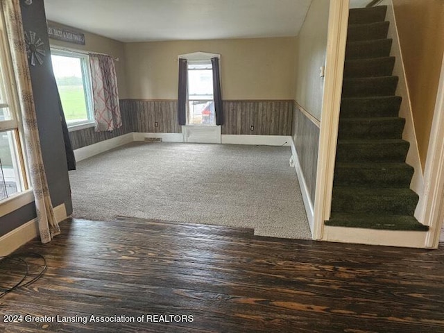 unfurnished room featuring a wealth of natural light, wainscoting, stairs, and dark carpet