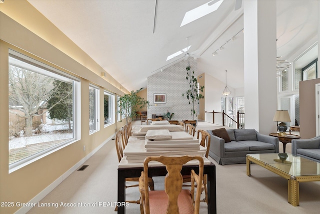 dining room featuring high vaulted ceiling, a skylight, rail lighting, carpet flooring, and a brick fireplace