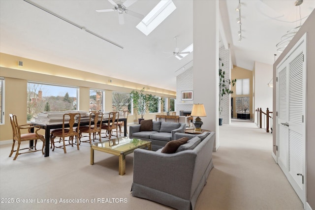 carpeted living room with rail lighting, a skylight, high vaulted ceiling, ceiling fan, and a fireplace