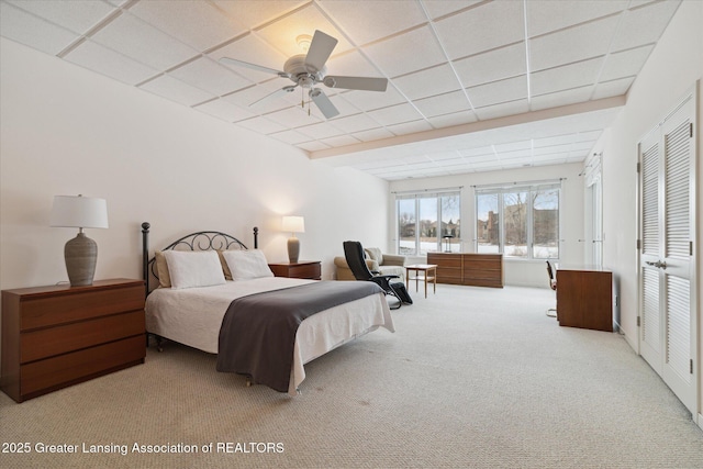 bedroom with a paneled ceiling, light colored carpet, and ceiling fan