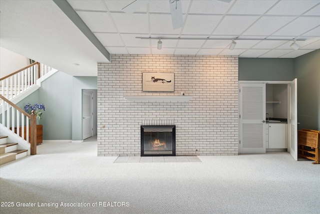 unfurnished living room featuring a fireplace, rail lighting, light carpet, and a drop ceiling