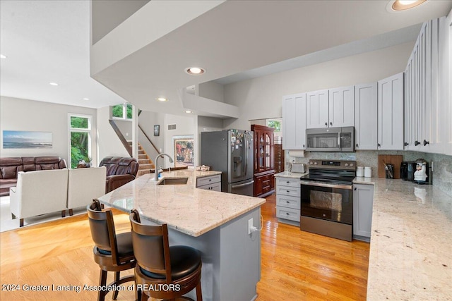 kitchen featuring appliances with stainless steel finishes, an island with sink, light stone countertops, and a breakfast bar