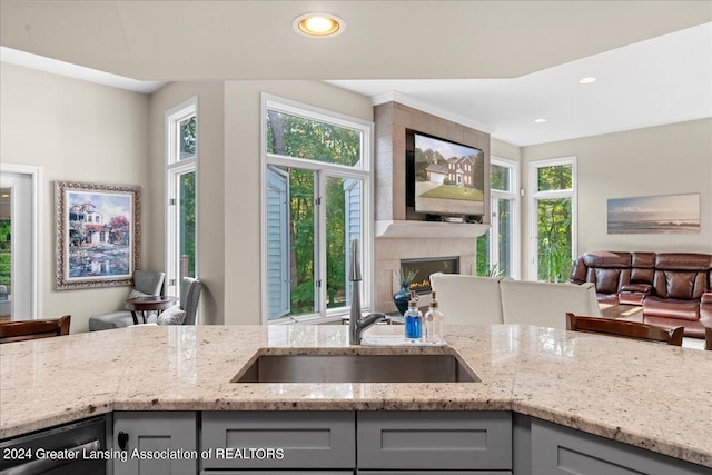 kitchen featuring a premium fireplace, light stone counters, sink, and gray cabinetry