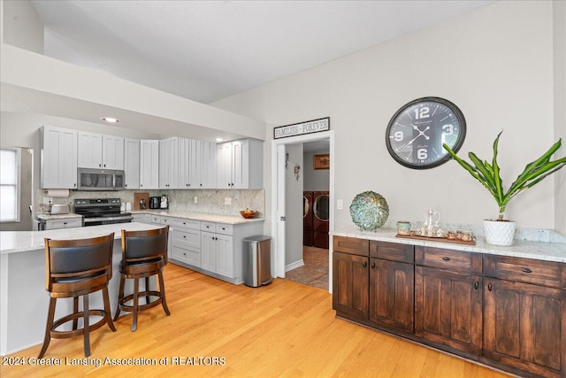 kitchen with light stone countertops, separate washer and dryer, a kitchen bar, stainless steel appliances, and light wood-type flooring