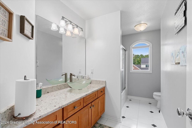 full bathroom featuring a textured ceiling, vanity, shower / bath combination with glass door, tile patterned flooring, and toilet