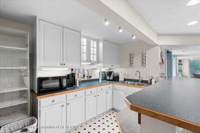 kitchen with white cabinetry, a wealth of natural light, kitchen peninsula, and sink