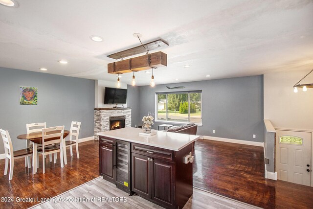 kitchen with dark hardwood / wood-style flooring, wine cooler, a stone fireplace, a kitchen island, and dark brown cabinetry