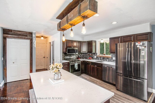 kitchen featuring pendant lighting, hardwood / wood-style floors, stainless steel appliances, sink, and decorative backsplash