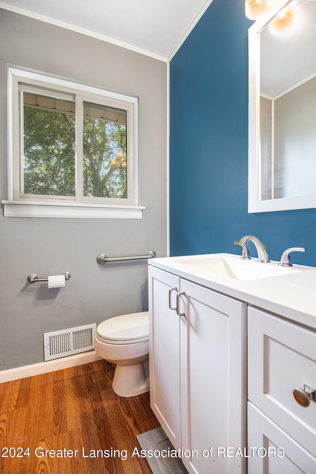 bathroom with wood-type flooring, toilet, ornamental molding, and vanity