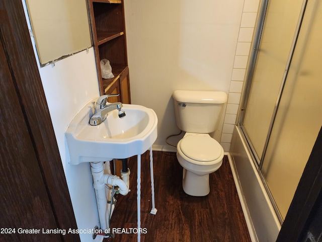 bathroom with wood-type flooring, bath / shower combo with glass door, and toilet