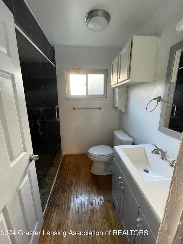 bathroom featuring wood-type flooring, vanity, toilet, and tiled shower