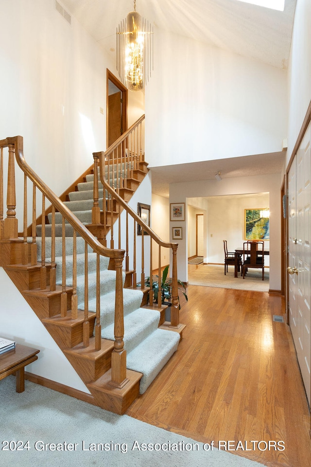 stairs with a high ceiling, a chandelier, and hardwood / wood-style flooring