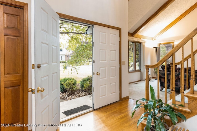 entrance foyer with lofted ceiling with beams and light hardwood / wood-style flooring