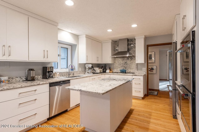 kitchen featuring wall chimney exhaust hood, light hardwood / wood-style floors, appliances with stainless steel finishes, and a kitchen island