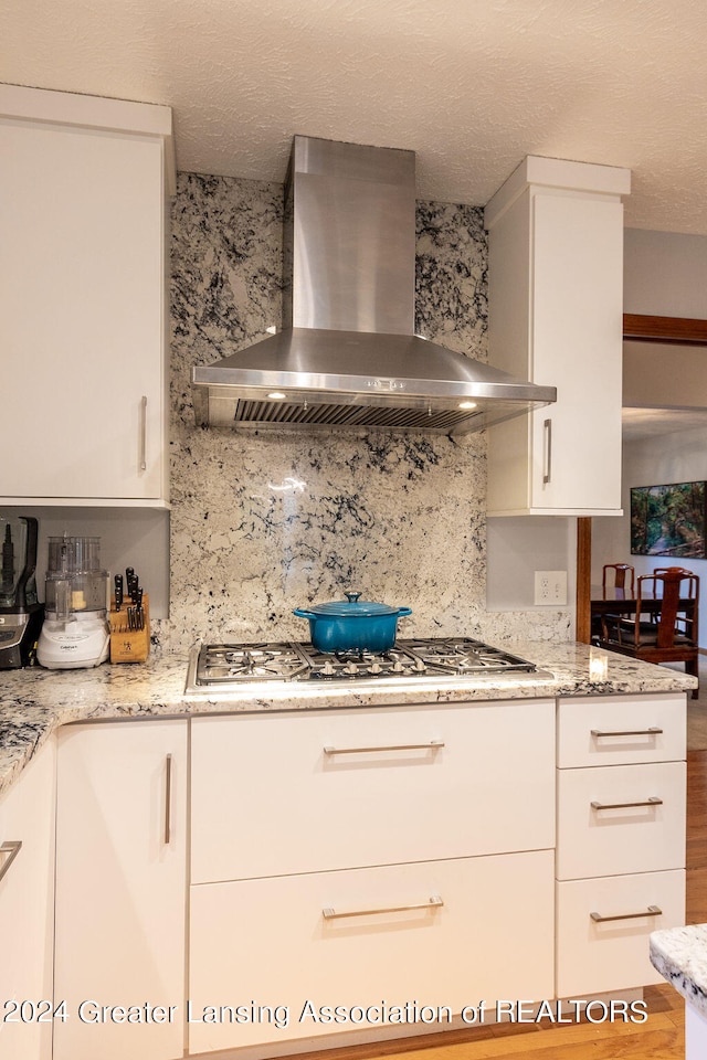 kitchen featuring light stone countertops, wall chimney exhaust hood, and white cabinetry