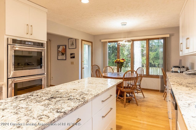 kitchen featuring double oven, light wood-type flooring, light stone countertops, and white cabinetry