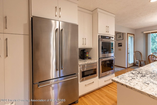 kitchen with white cabinetry, light stone countertops, stainless steel appliances, a textured ceiling, and light hardwood / wood-style flooring