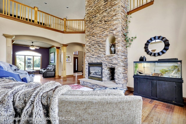 living room with wood-type flooring, ceiling fan, a high ceiling, and a fireplace