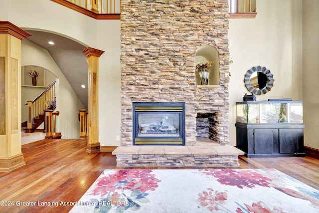 living room featuring ornate columns, a high ceiling, hardwood / wood-style floors, and a stone fireplace