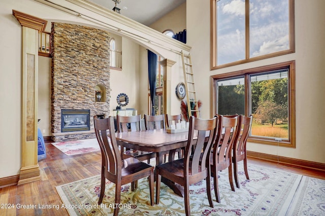 dining area featuring a stone fireplace, a towering ceiling, and hardwood / wood-style floors