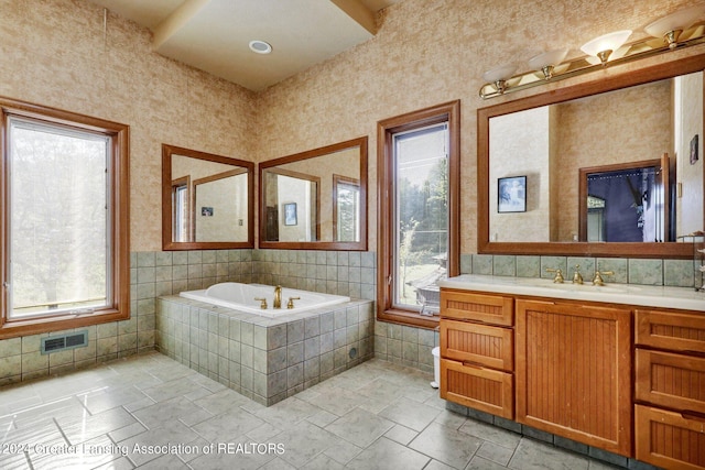 bathroom featuring vanity, tiled bath, plenty of natural light, and tile walls