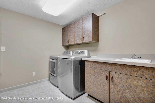 laundry area with cabinets, a textured ceiling, sink, washing machine and clothes dryer, and light tile patterned floors