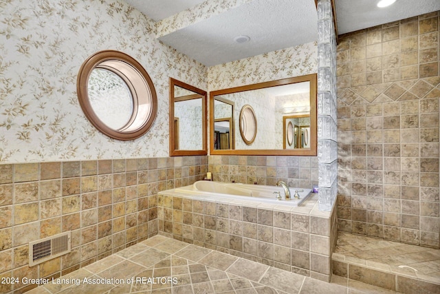 bathroom with tiled tub and a textured ceiling