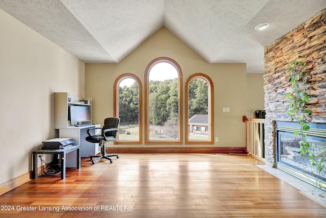 office with light hardwood / wood-style flooring, lofted ceiling, a textured ceiling, and a fireplace