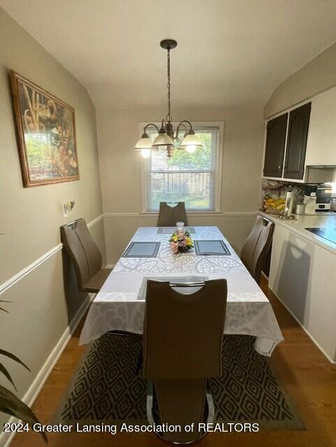 dining room with a notable chandelier, dark wood-type flooring, and vaulted ceiling