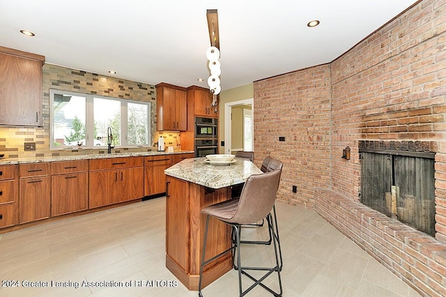 kitchen with light stone counters, a center island, a breakfast bar area, stainless steel double oven, and a fireplace