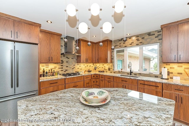 kitchen featuring pendant lighting, sink, backsplash, wall chimney range hood, and appliances with stainless steel finishes