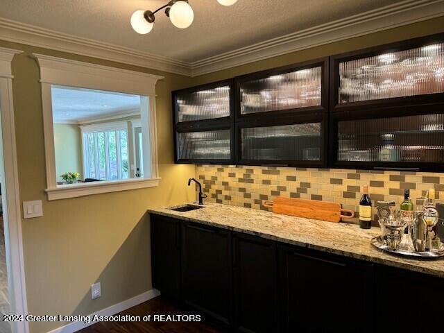 bar featuring ornamental molding, decorative backsplash, light stone counters, and sink