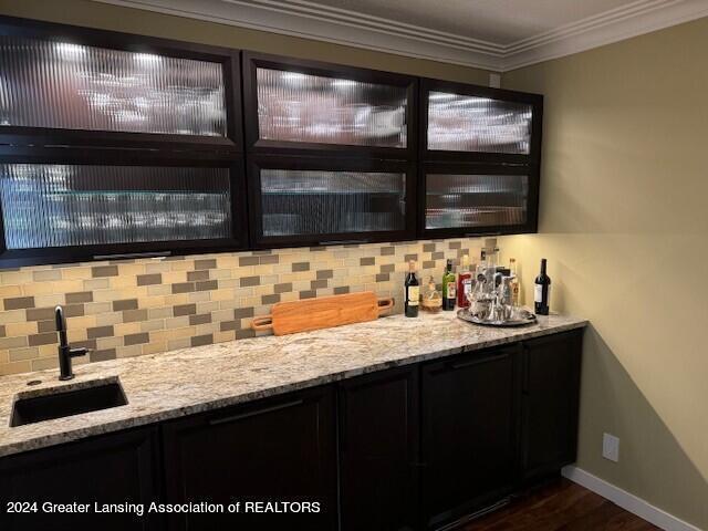 bar featuring light stone countertops, crown molding, sink, and decorative backsplash