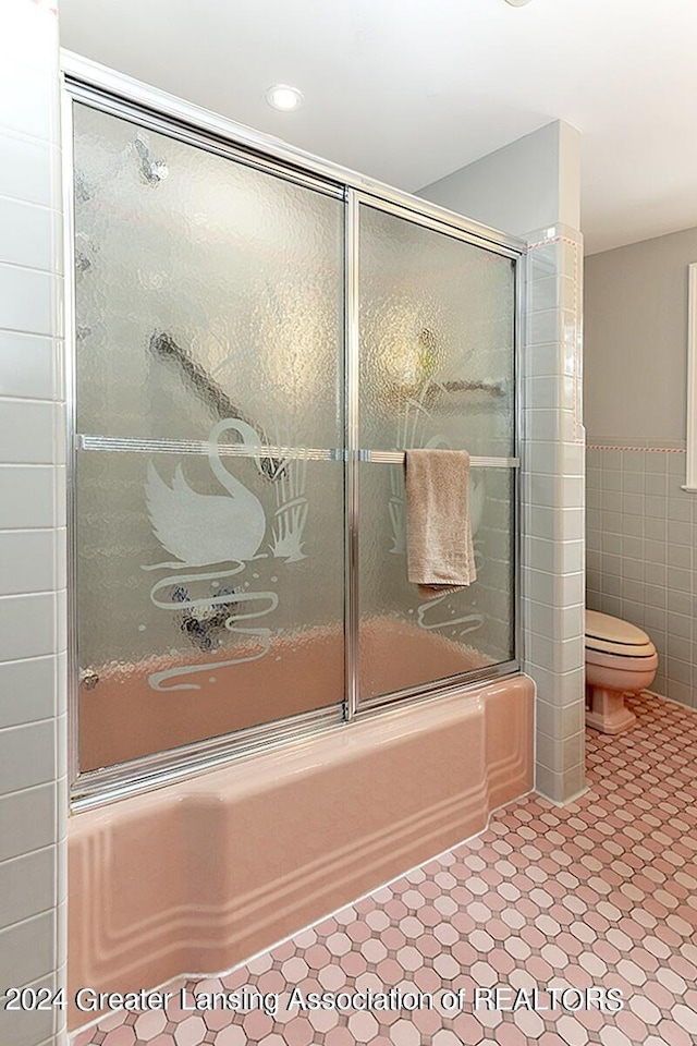 bathroom with tile walls, bath / shower combo with glass door, toilet, and tile patterned floors