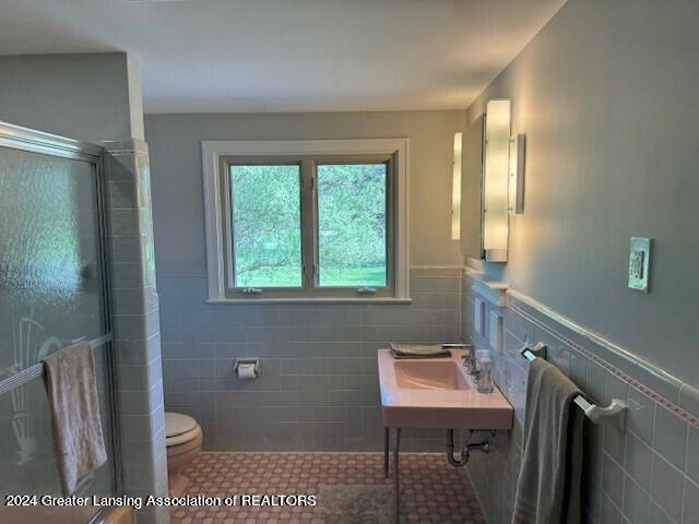 bathroom with tile walls, toilet, an enclosed shower, and tile patterned floors