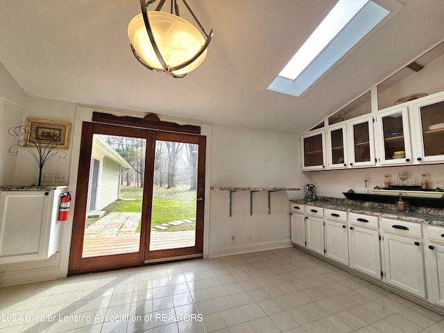 kitchen featuring dark stone countertops, white cabinets, light tile patterned floors, pendant lighting, and vaulted ceiling with skylight