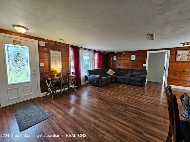 living room with wooden walls, a textured ceiling, and dark hardwood / wood-style floors