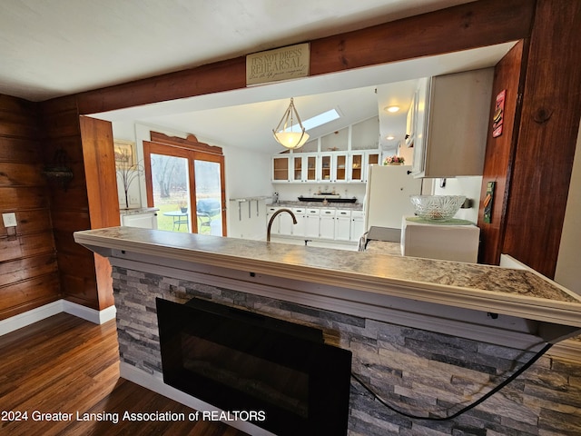 kitchen featuring pendant lighting, vaulted ceiling with skylight, dark hardwood / wood-style floors, sink, and a stone fireplace