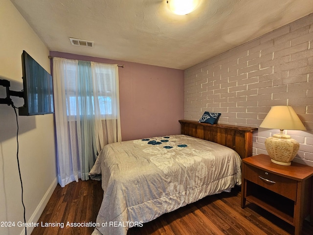 bedroom featuring brick wall, a textured ceiling, and dark wood-type flooring