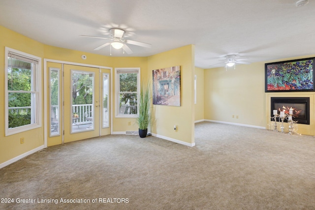 unfurnished living room with ceiling fan, light colored carpet, and plenty of natural light