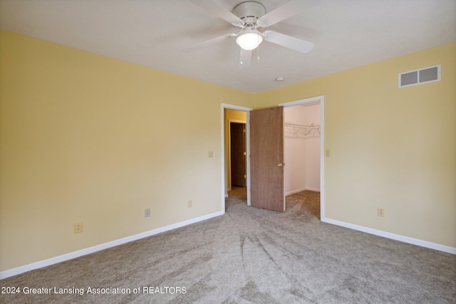 unfurnished bedroom featuring a spacious closet, a closet, ceiling fan, and light carpet