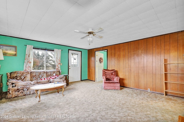 unfurnished living room featuring ceiling fan, wood walls, and carpet