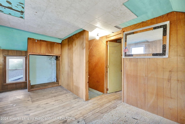 additional living space with wooden walls, light hardwood / wood-style floors, and lofted ceiling