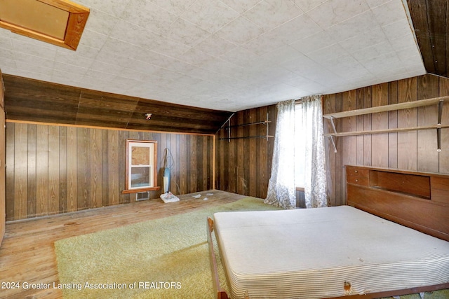 unfurnished bedroom featuring hardwood / wood-style flooring, wooden walls, and vaulted ceiling