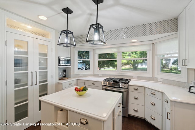 kitchen featuring dark wood-type flooring, white cabinets, stainless steel appliances, a center island, and decorative light fixtures