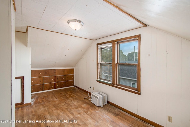 additional living space with vaulted ceiling, a wall unit AC, wood walls, and hardwood / wood-style flooring