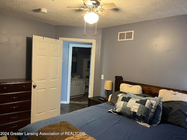 bedroom with ceiling fan, a textured ceiling, dark hardwood / wood-style floors, ensuite bath, and sink