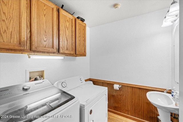 laundry area with light hardwood / wood-style floors, wood walls, cabinets, sink, and washer and dryer